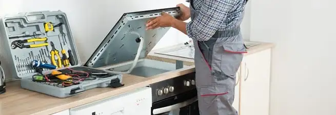 Cooktop repair technician lifting a built-in stovetop for service in San Diego, CA