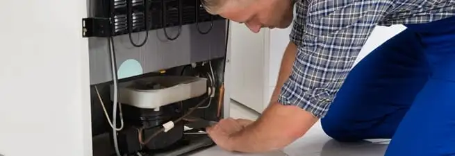 Refrigerator repair technician servicing the compressor and condenser area in San Diego, CA