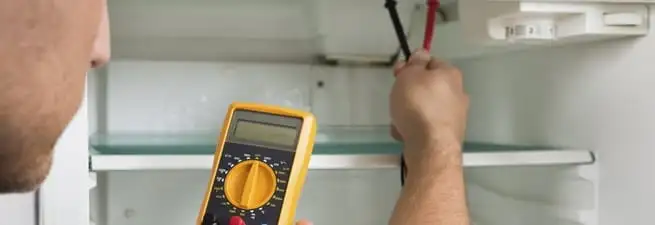 Refrigerator repair technician testing electrical components with a multimeter in San Diego, CA